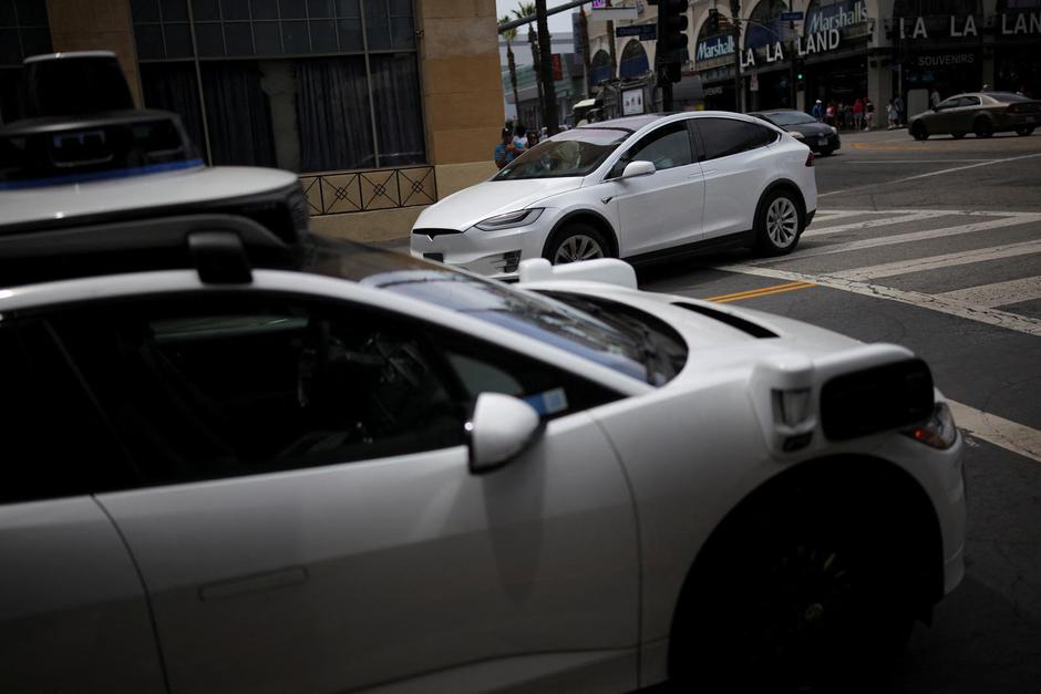 A Tesla drives by a Waymo self-driving car in Los Angeles | Author: DANIEL COLE/REUTERS