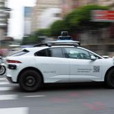 Police officers riding motorcycles follow a Waymo driverless vehicle as it drives through downtown Los Angeles